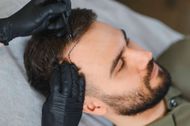 Behandschuhte Hände formen mit Haarschneidemaschinen den Haaransatz eines Mannes während eines Bart- und Haarschnittservices