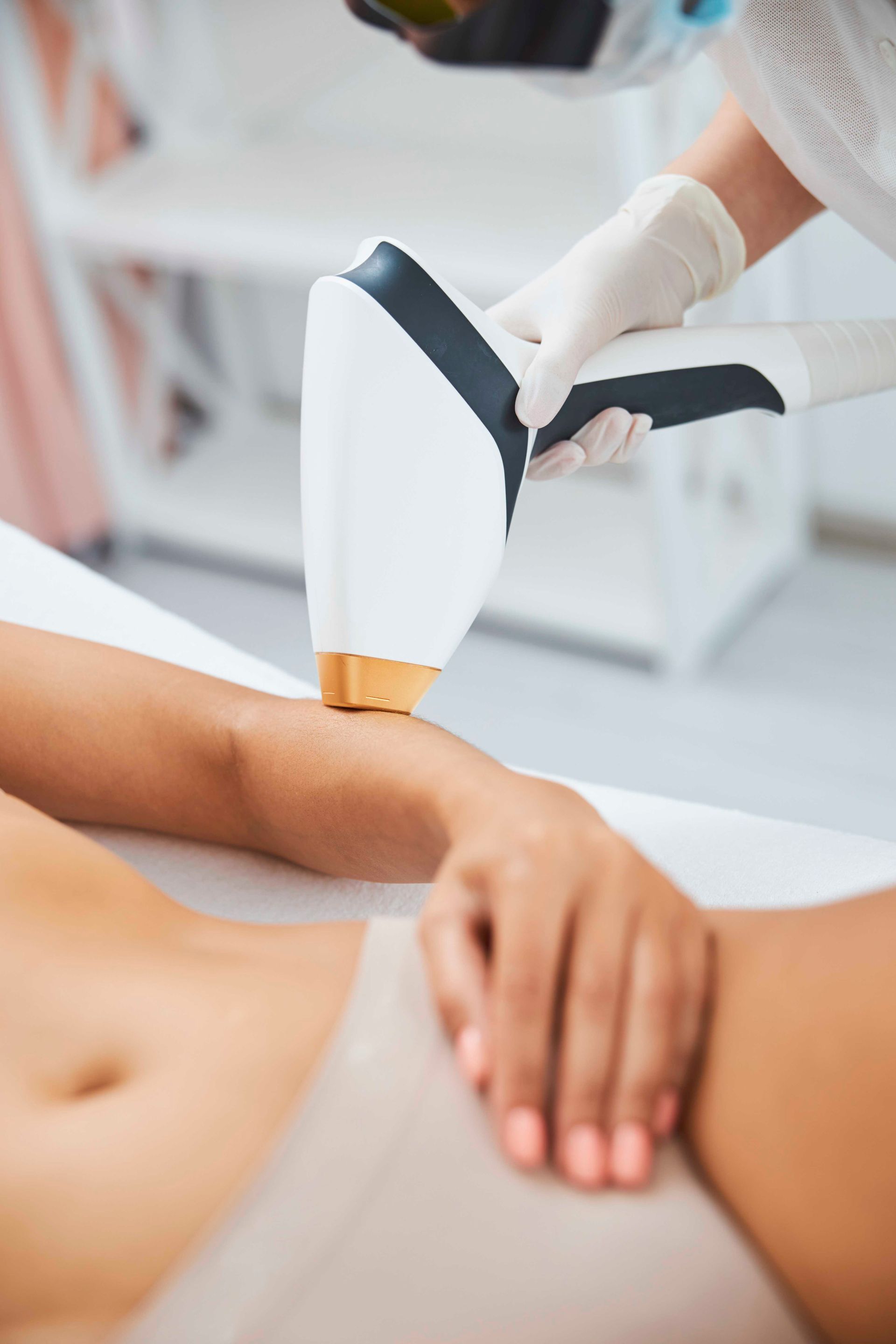 Laserhaarentfernung am Bein einer Person mit einem Handgerät in einer Klinik