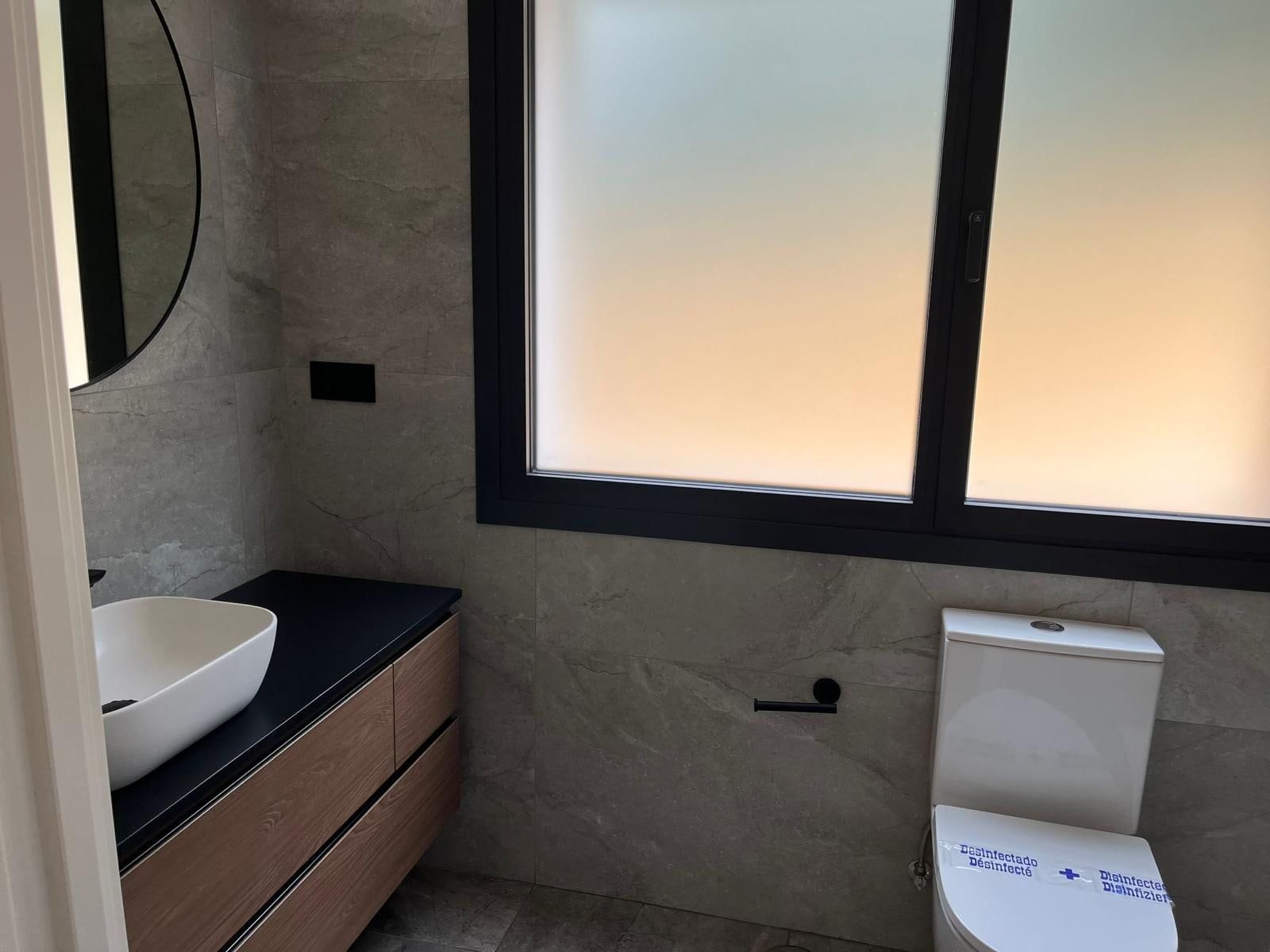 Baño con paredes de baldosas de piedra, tocador de madera y ventana esmerilada.