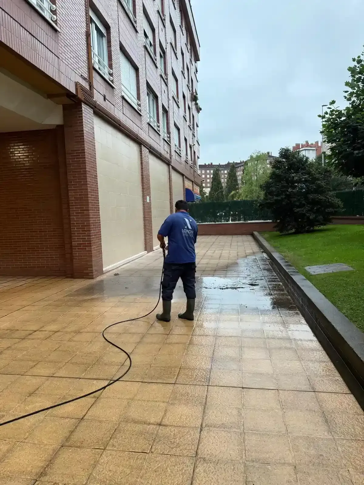 Una persona lava a presión un patio de baldosas afuera de un edificio de ladrillos.