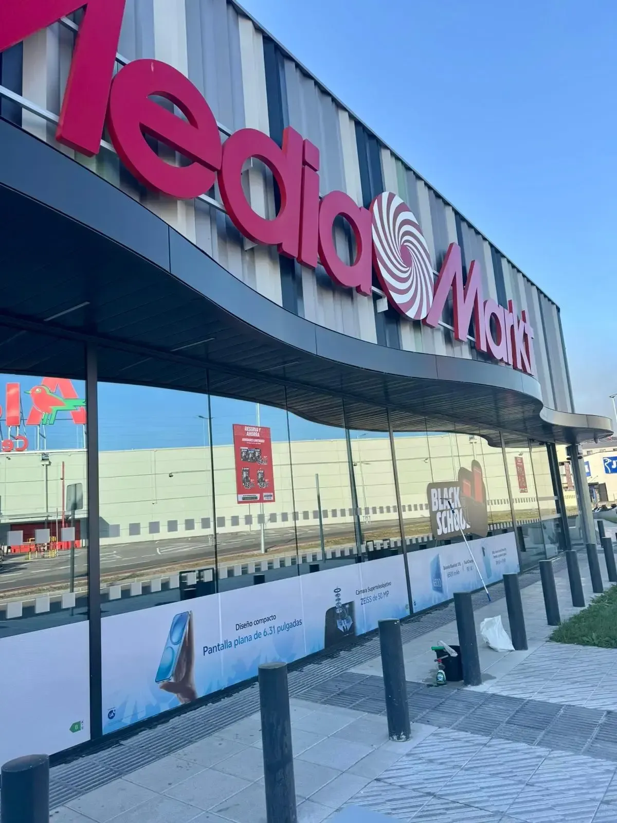 Exterior de la tienda MediaMarkt con logotipo rojo y cielo reflejado. Edificio moderno con anuncios.