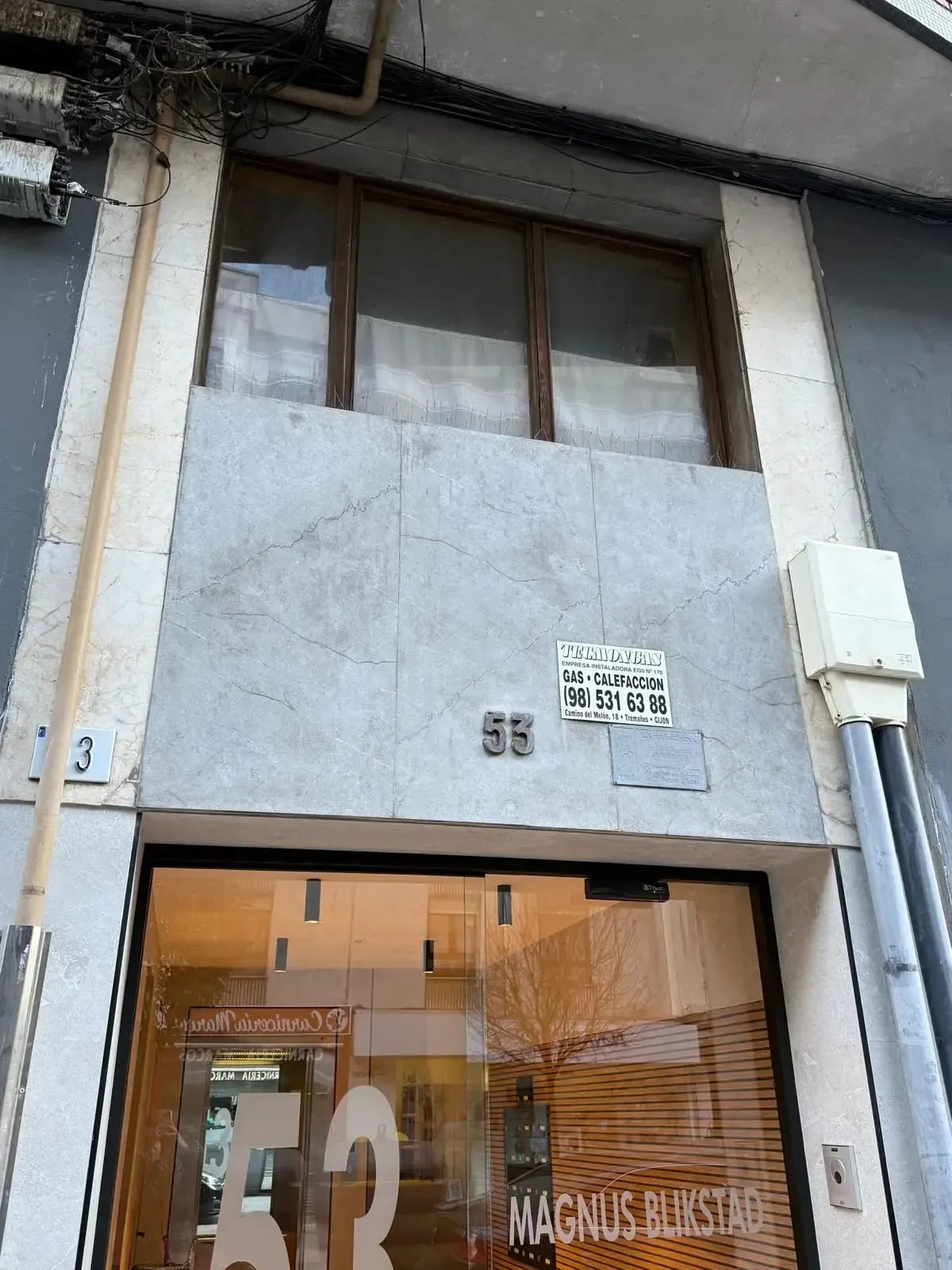 Vista exterior del edificio 5E sobre la entrada acristalada. Fachada gris con ventanas en la parte superior.