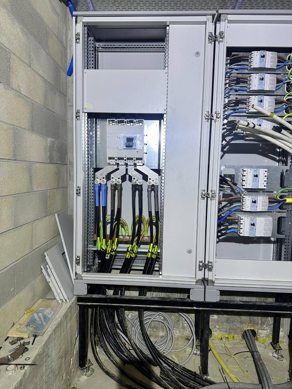 Armoire électrique à portes ouvertes, laissant apparaître le câblage et les composants contre un mur en parpaings.