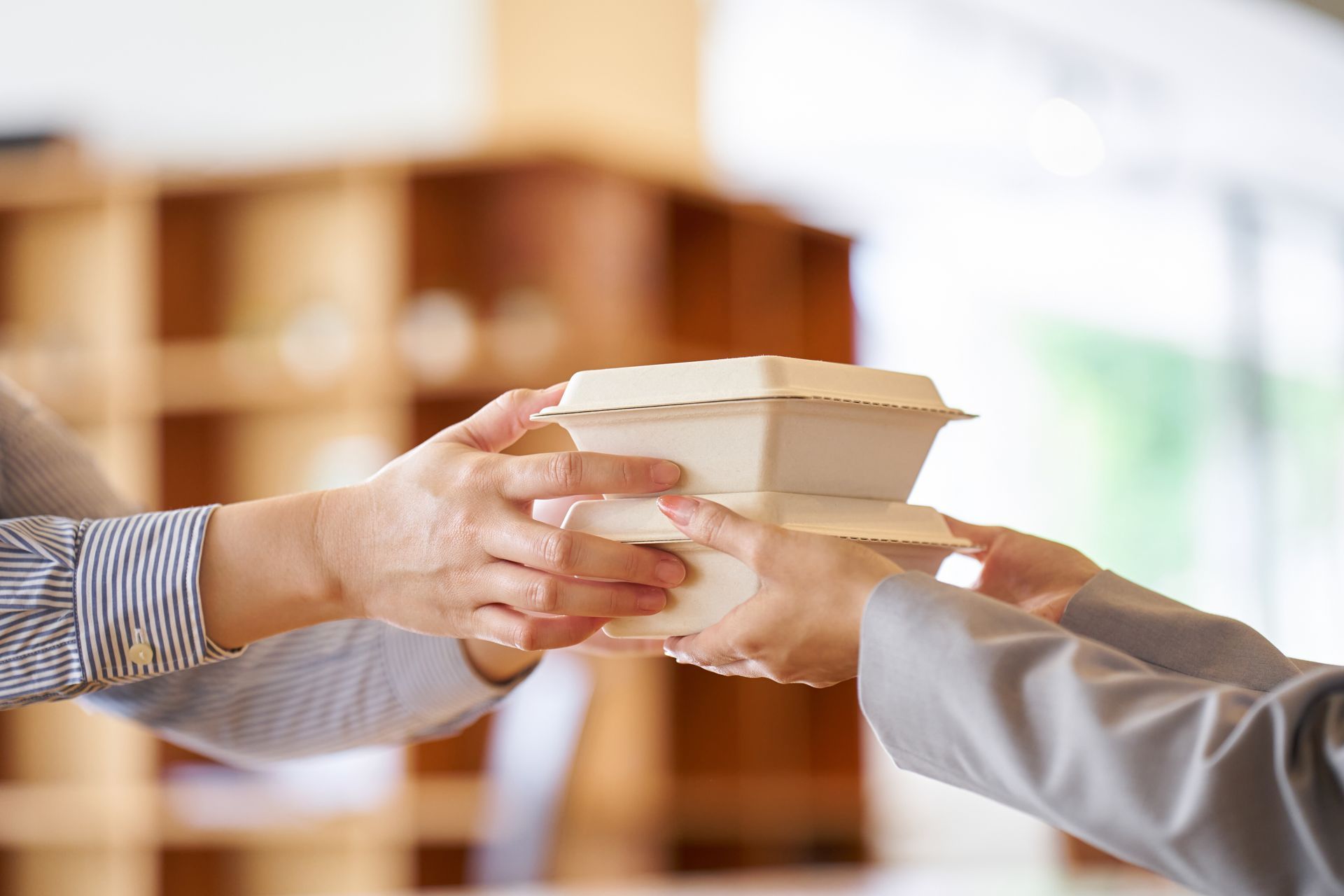Des mains se passent deux boîtes à emporter en carton dans un restaurant.