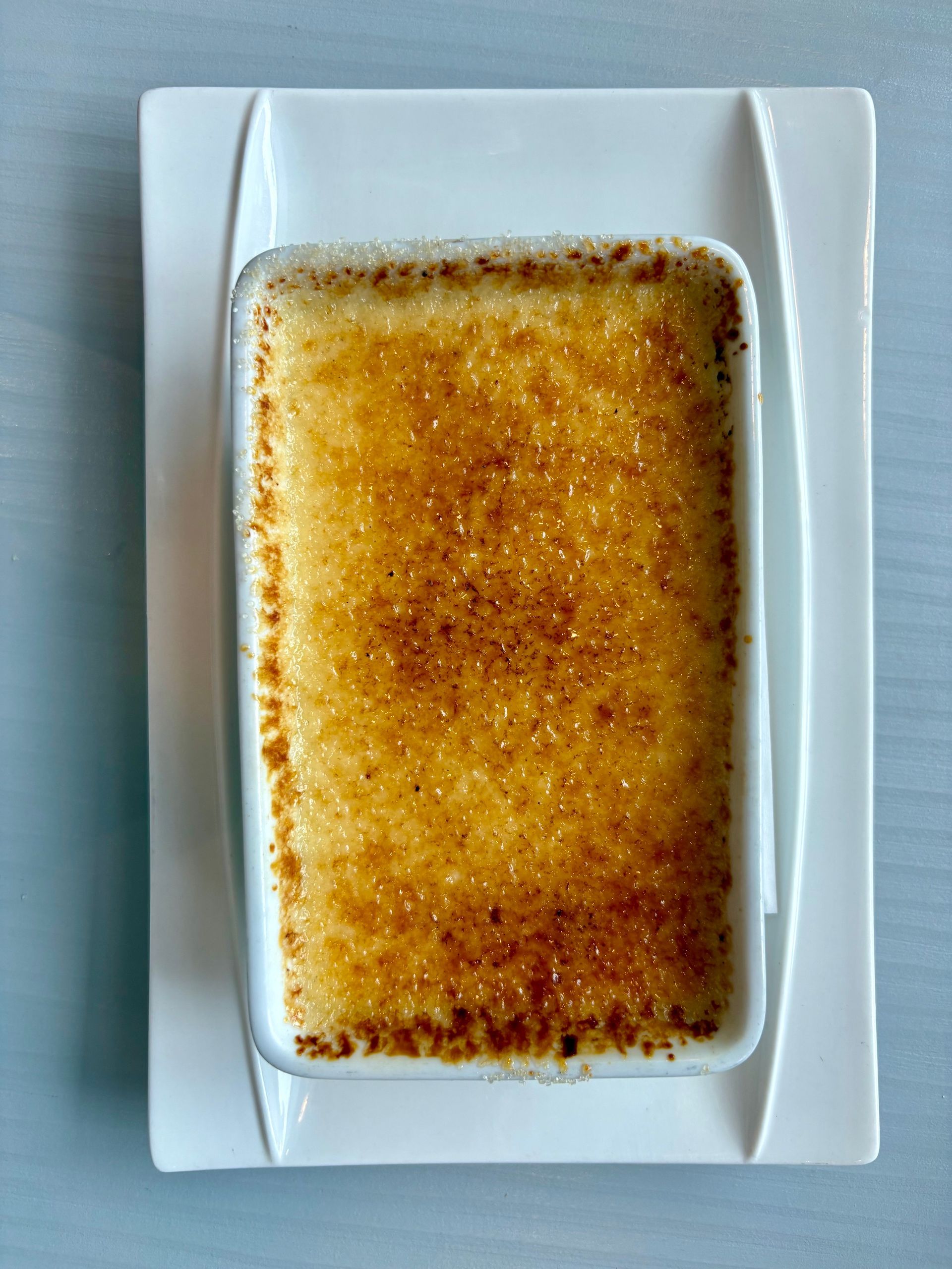 Crème brûlée rectangulaire dans un plat blanc sur une assiette blanche, nappée de sucre caramélisé
