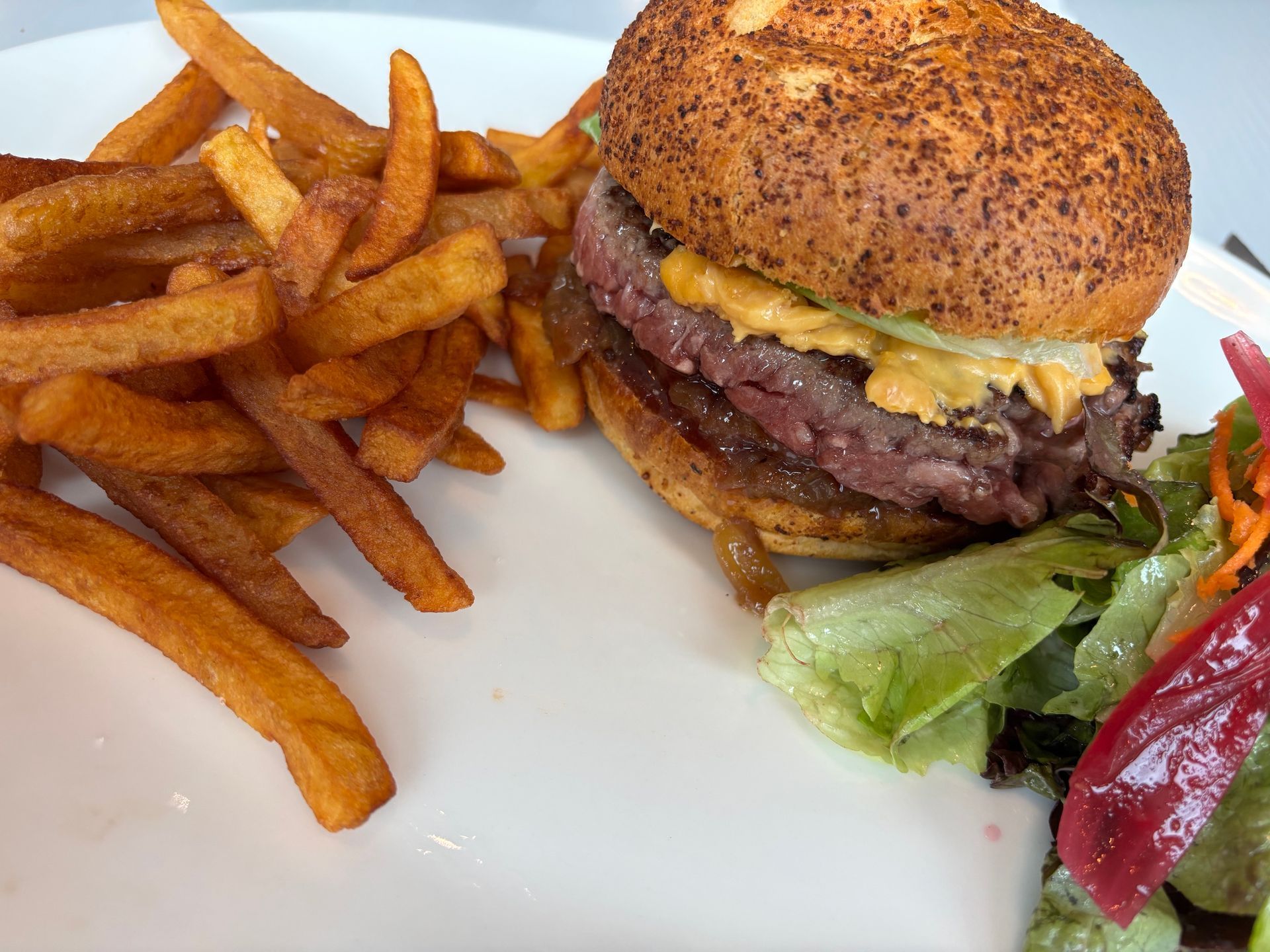 Burger avec frites sur une assiette blanche, accompagné de laitue et d'une salade.