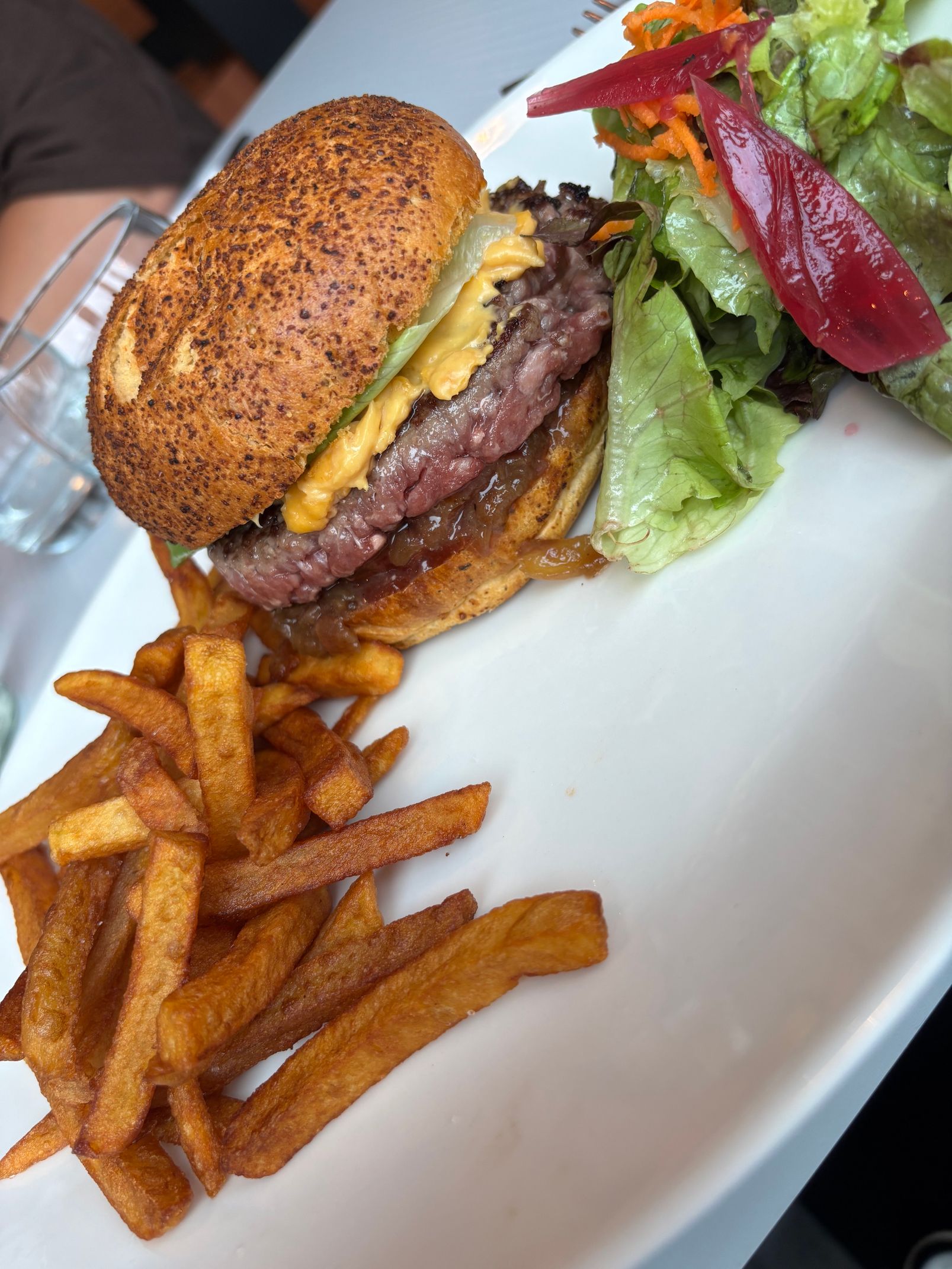Burger, frites et salade d'accompagnement sur une assiette blanche, avec un pain grillé et du fromage fondu