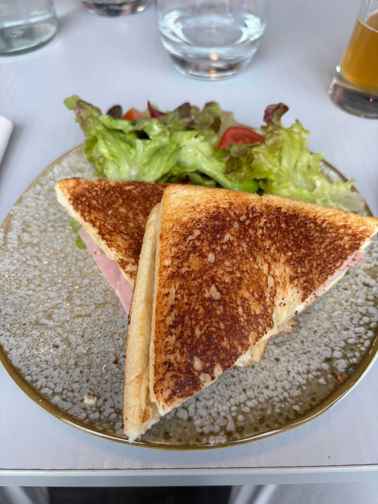 Des triangles de sandwich grillés sur une assiette avec une salade verte à côté, sur une table blanche
