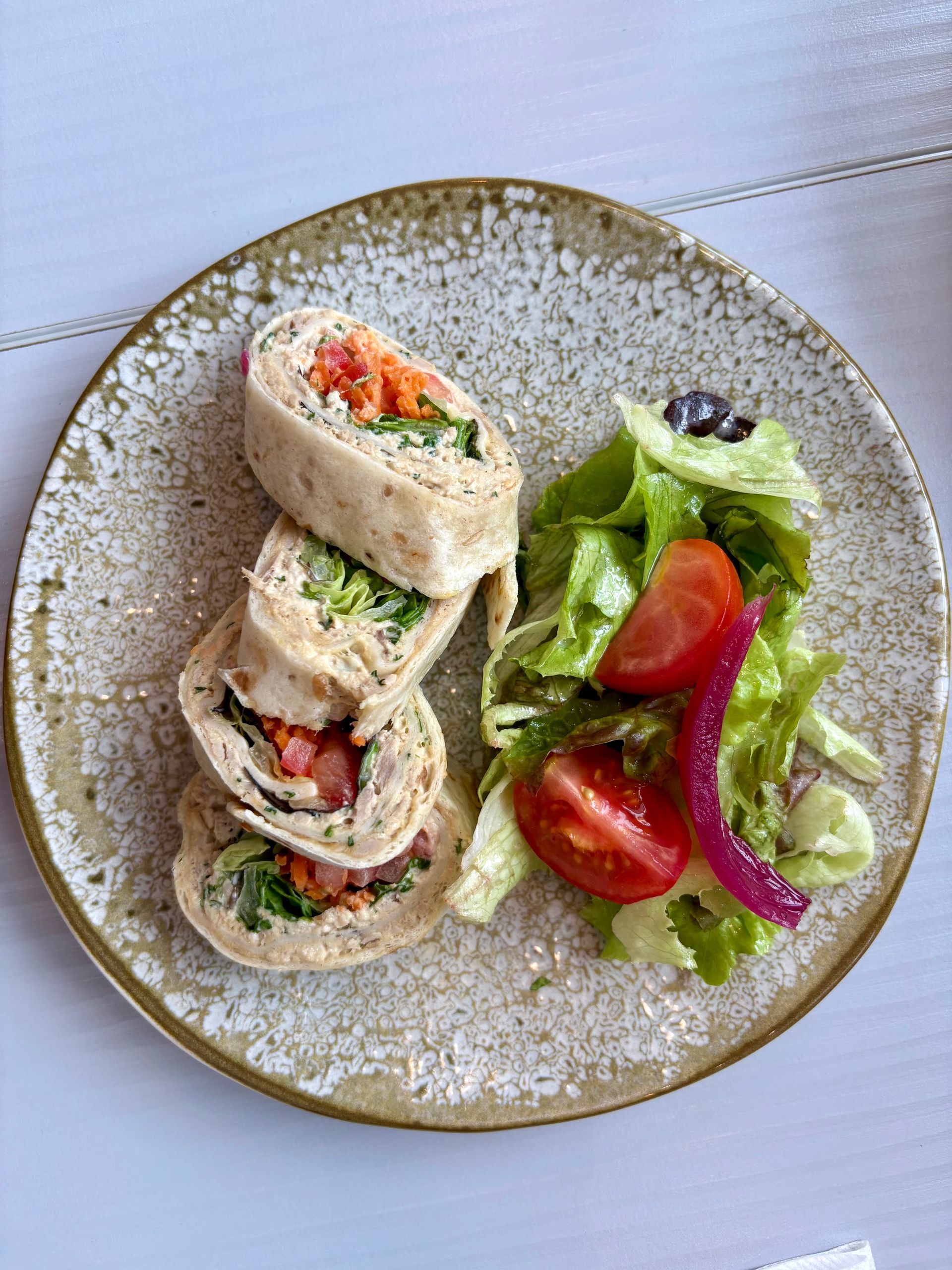 Assiette avec des galettes coupées en tranches et une salade verte avec tomates et oignons sur un plat moucheté