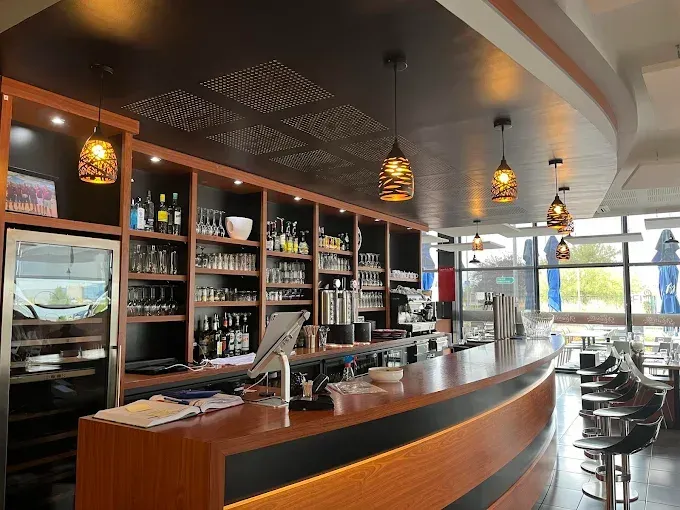 Bar de Chez Meurette avec comptoir en bois, étagères de verres et suspensions lumineuses.