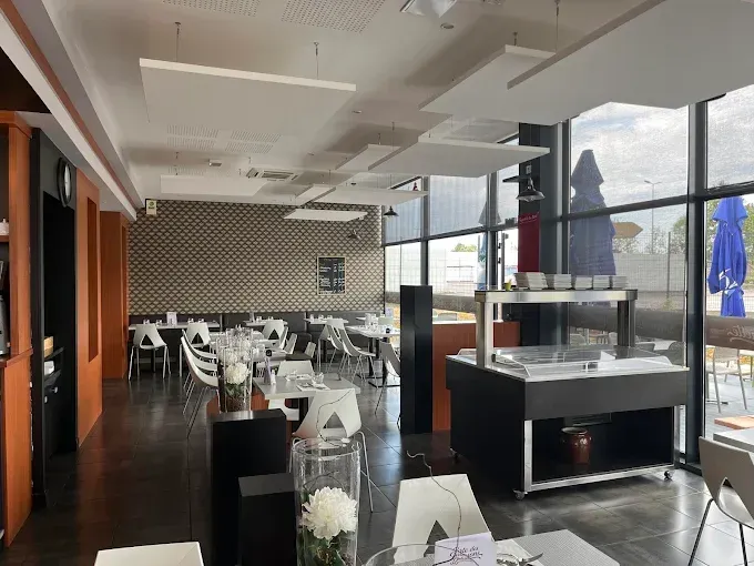 Salle à manger moderne d'un restaurant avec chaises et tables blanches, et de grandes fenêtres.
