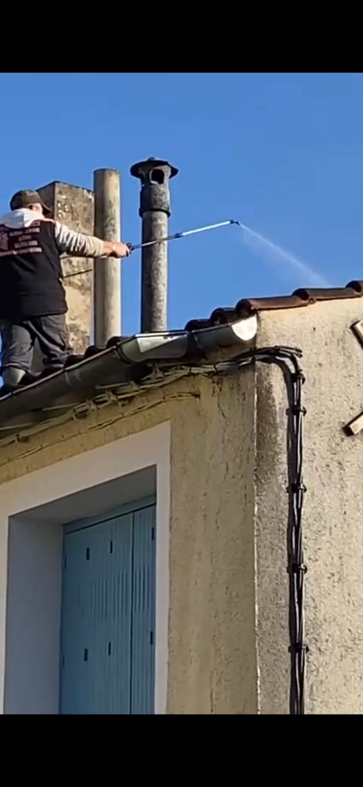 Une personne sur un toit pulvérise un traitement antimousse.