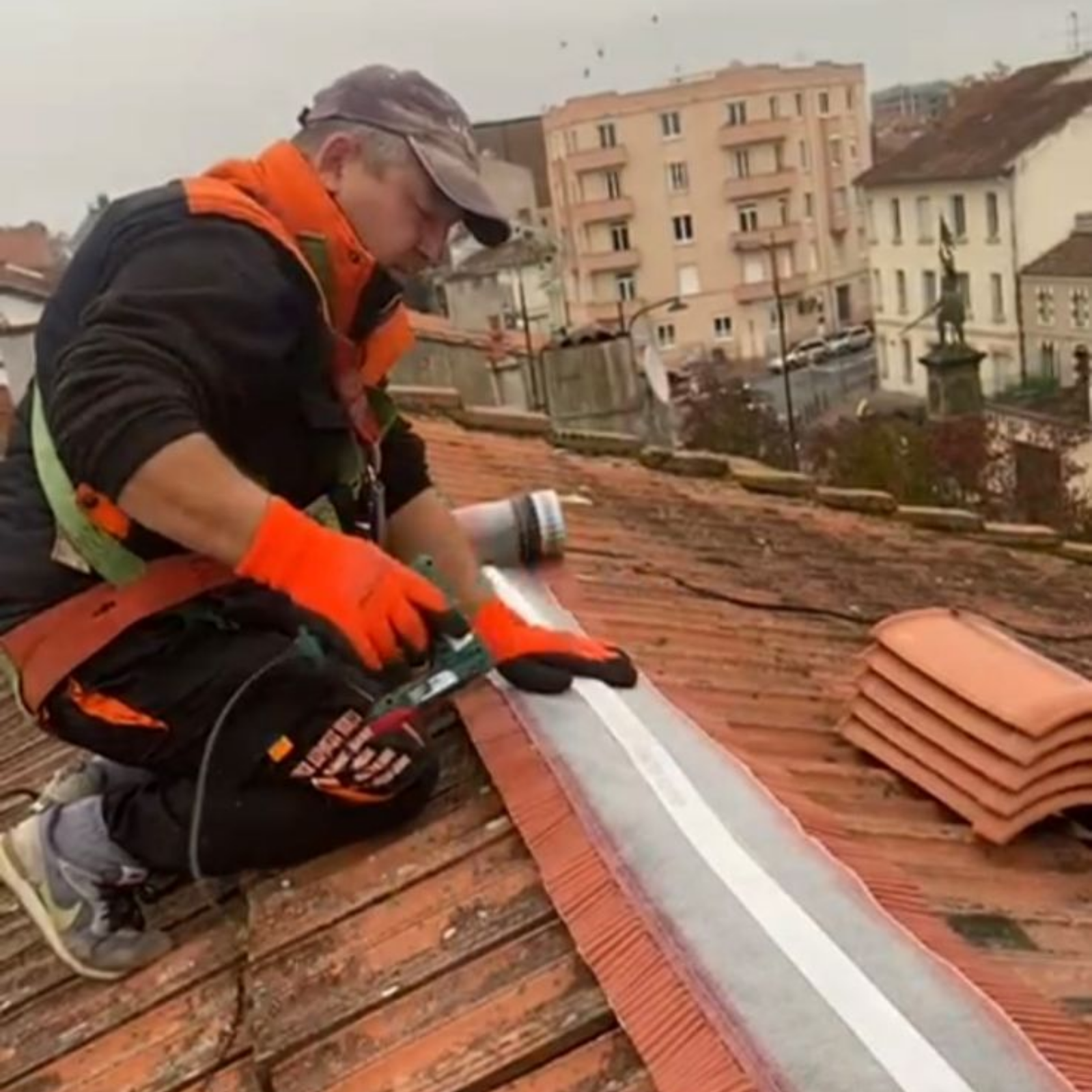 Couvreur calfeutrant le faîtage d'un toit en ville.