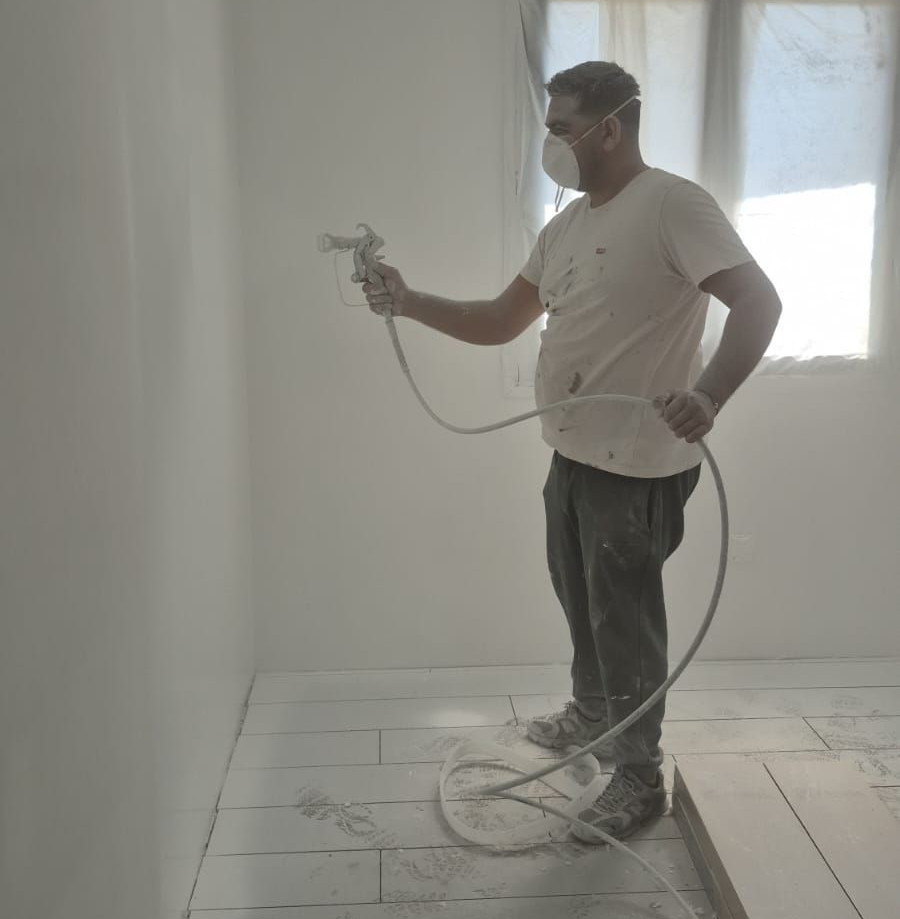 Un homme portant un masque pulvérise de la peinture blanche sur un mur.