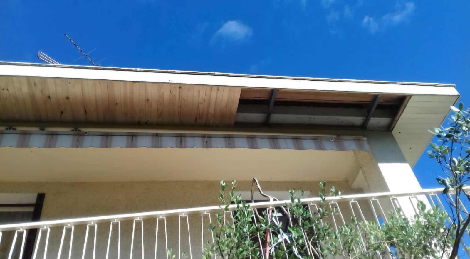 Sous-face en bois endommagée sur un bâtiment, révélant la structure intérieure. Ciel bleu en arrière-plan.