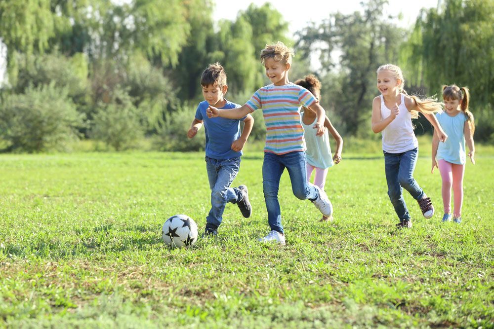 Kinder spielen an einem sonnigen Tag in einem grasbewachsenen Park Fußball.