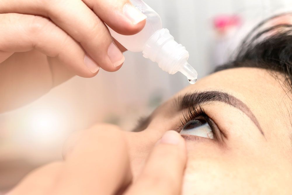 Person, die sich im Innenbereich Augentropfen ins Auge gibt.