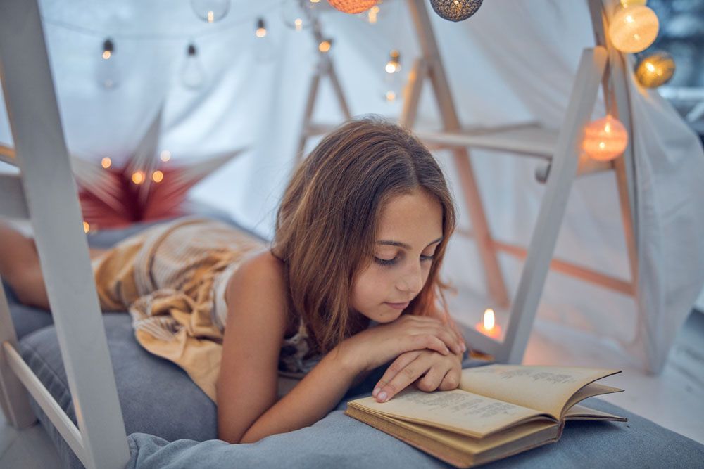 Mädchen liest ein Buch in einer gemütlichen Festung, beleuchtet von Lichterketten.