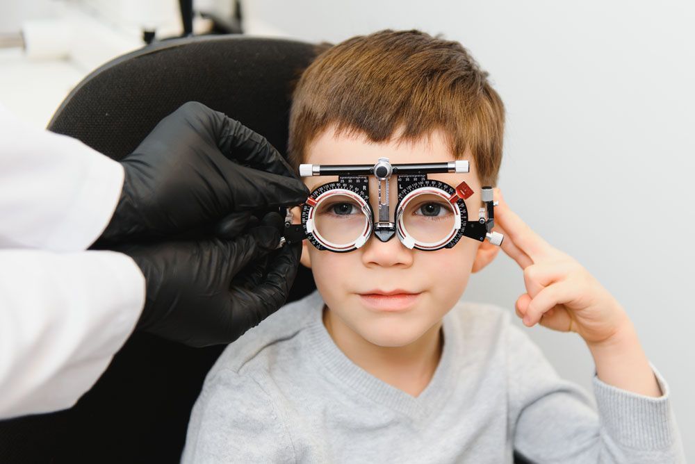 Junge bei einer Augenuntersuchung; Optiker passt die Brillenfassung an. Innenaufnahme.