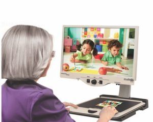 Frau, die eine Videolupe verwendet und Kindern beim Zeichnen zusieht.