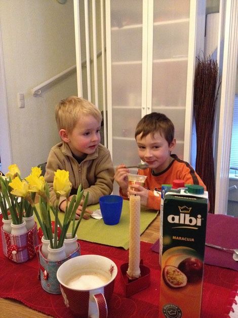 Zwei junge Jungen an einem Tisch mit Getränken, Snacks, Blumen und Saft. Einer der Jungen lächelt.
