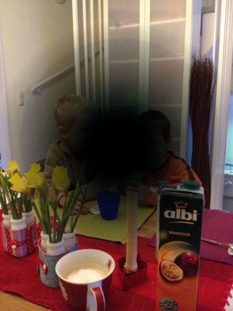 Zwei Kinder an einem schwarz verdunkelten Tisch mit Saft, Blumen und einer Kaffeetasse.