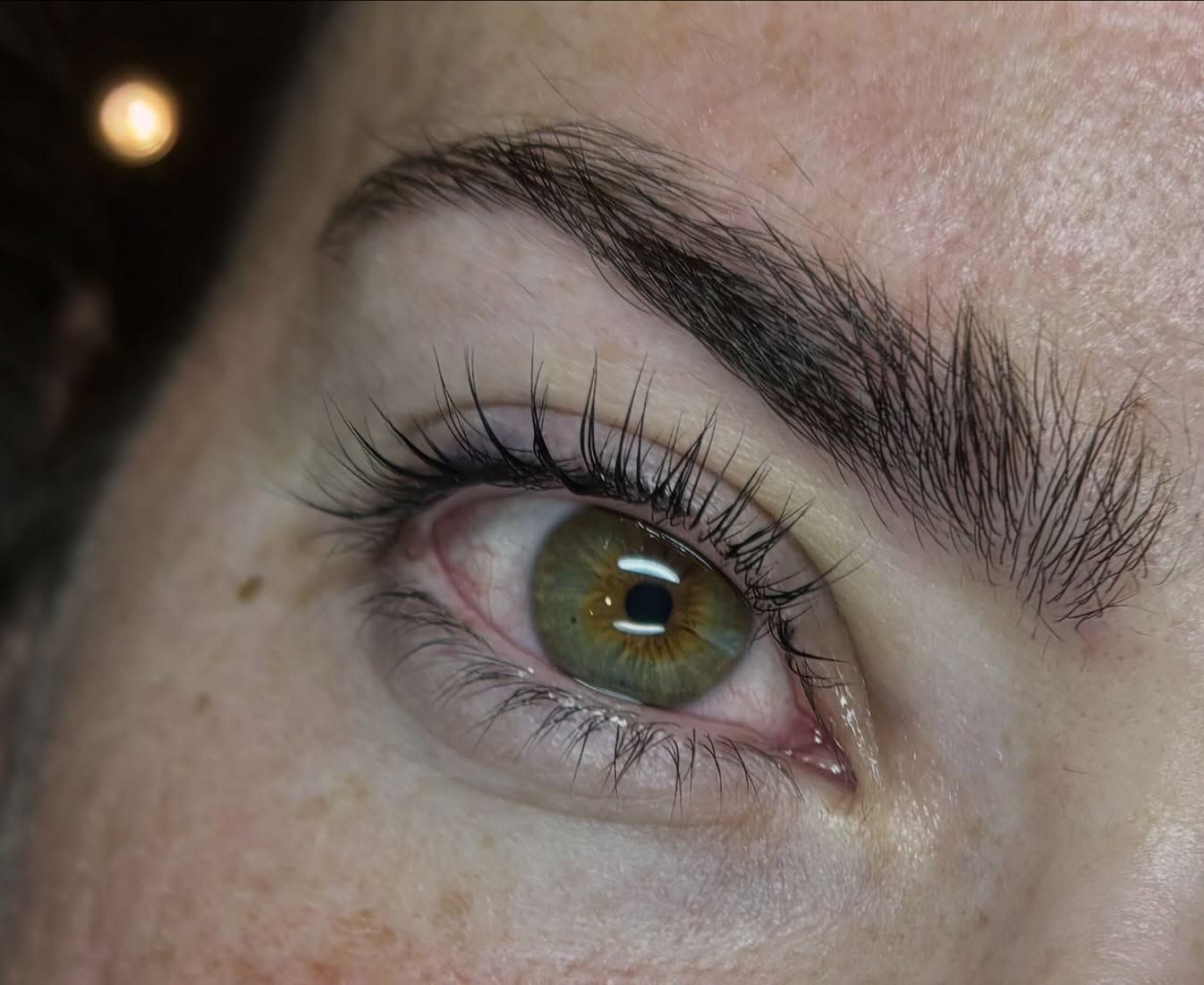 Primer plano de un ojo color verde avellana con pestañas y ceja visibles.