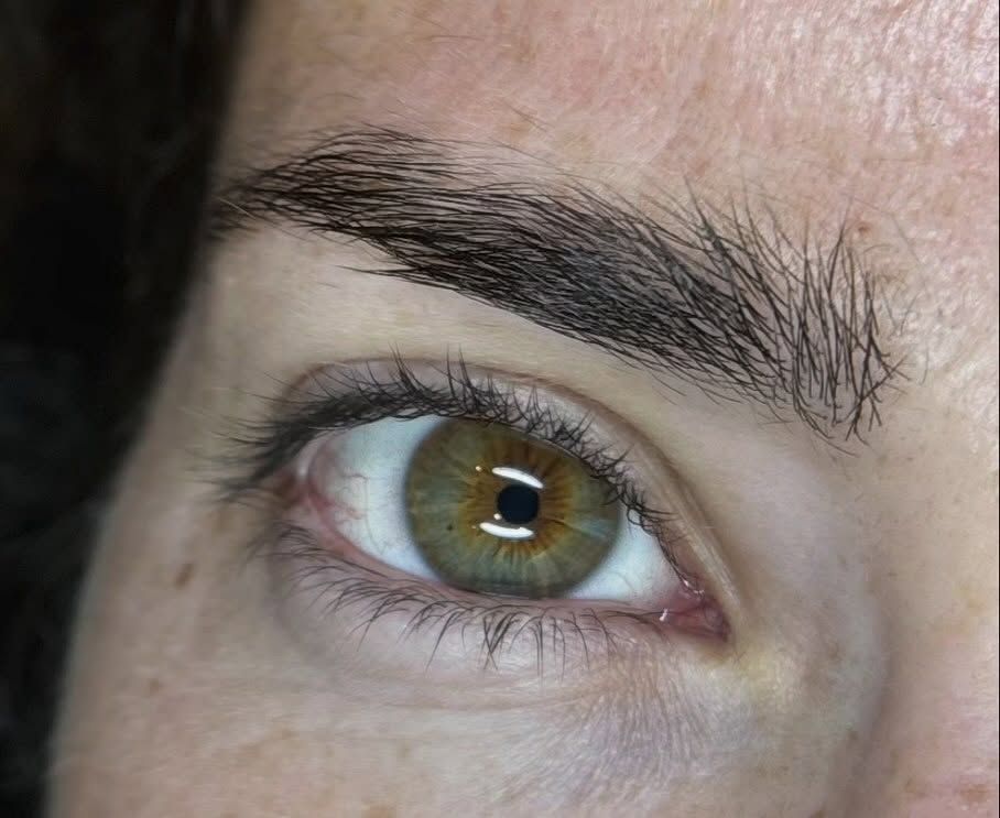 Primer plano de un ojo con iris color avellana verdoso y centro marrón, situado debajo de una ceja oscura y bien arreglada.