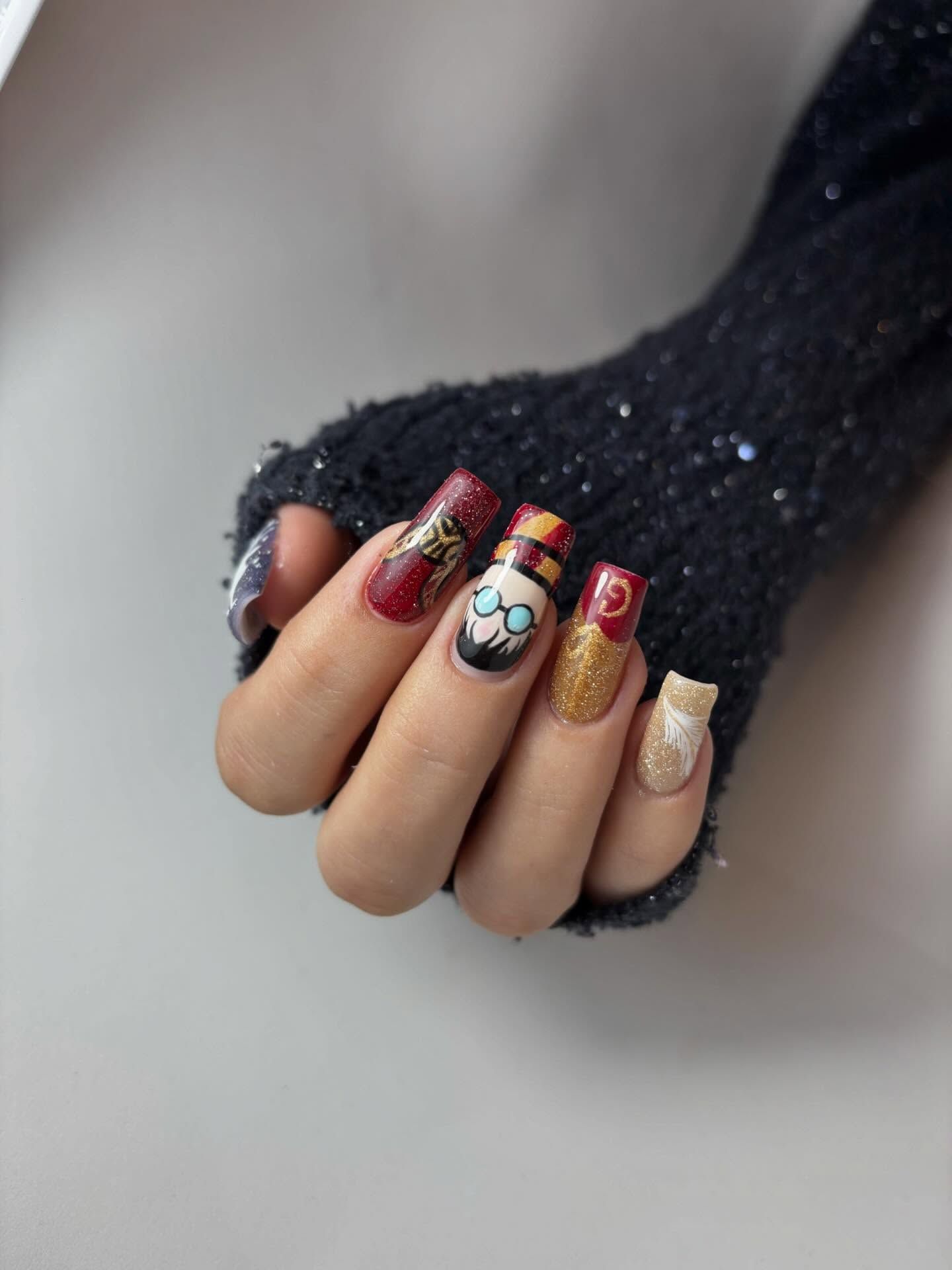Mano con uñas cuadradas decoradas con motivos de Harry Potter, incluyendo un retrato, purpurina dorada y detalles granates.
