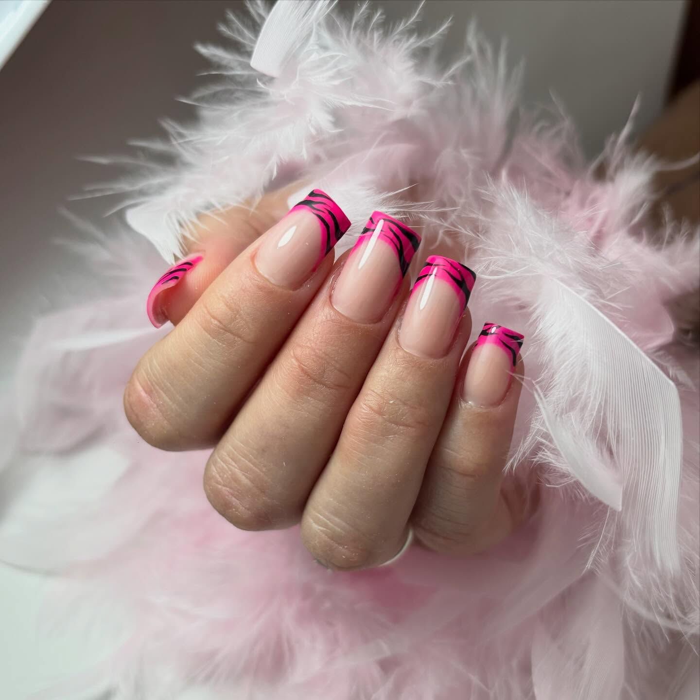 Mano con manicura francesa en puntas rosas y estampado de cebra negro, descansando sobre suaves plumas de color rosa claro.