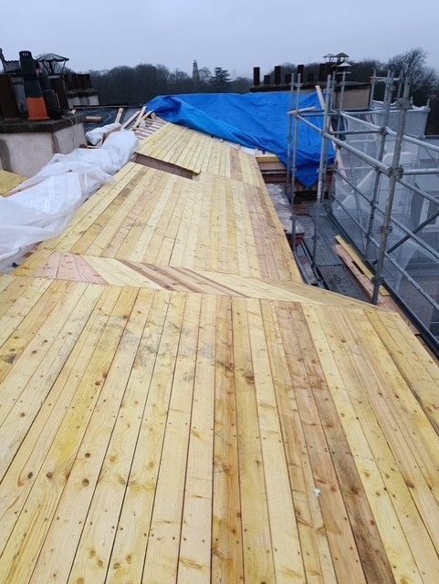 Passerelle en bois sur le toit en construction, avec des bâches bleues et des échafaudages sur la droite