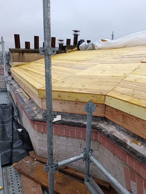 Toiture en construction avec panneaux isolants jaunes et échafaudages le long d'un parapet en briques