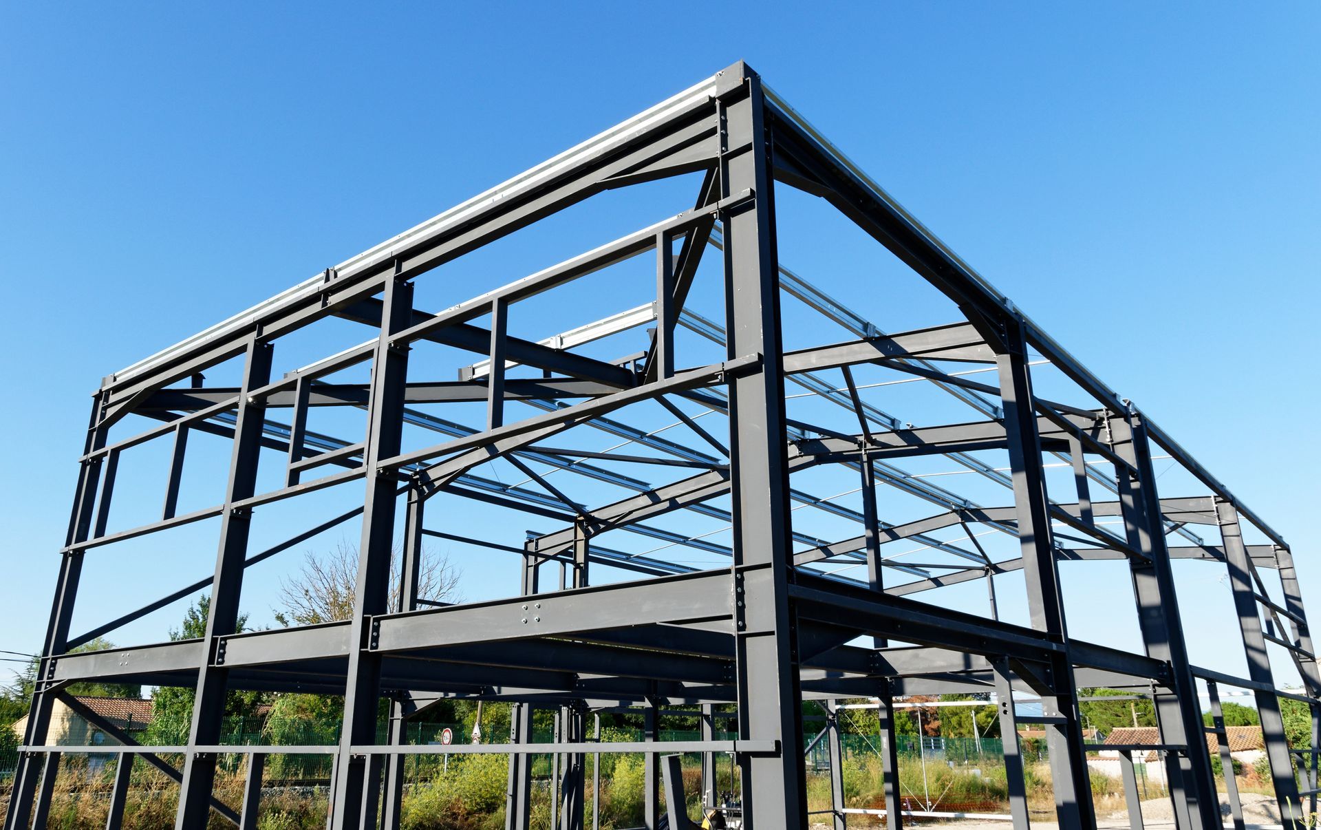 La structure en acier noir d'un bâtiment en construction se détache sur un ciel bleu.