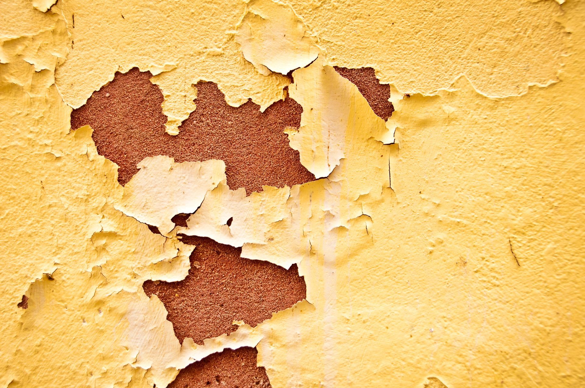 Peinture jaune écaillée révélant un mur brun en dessous