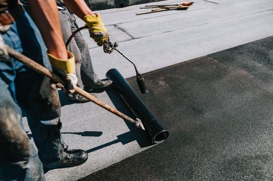 Des ouvriers utilisent un rouleau pour appliquer un revêtement de toiture noir sur un toit plat.