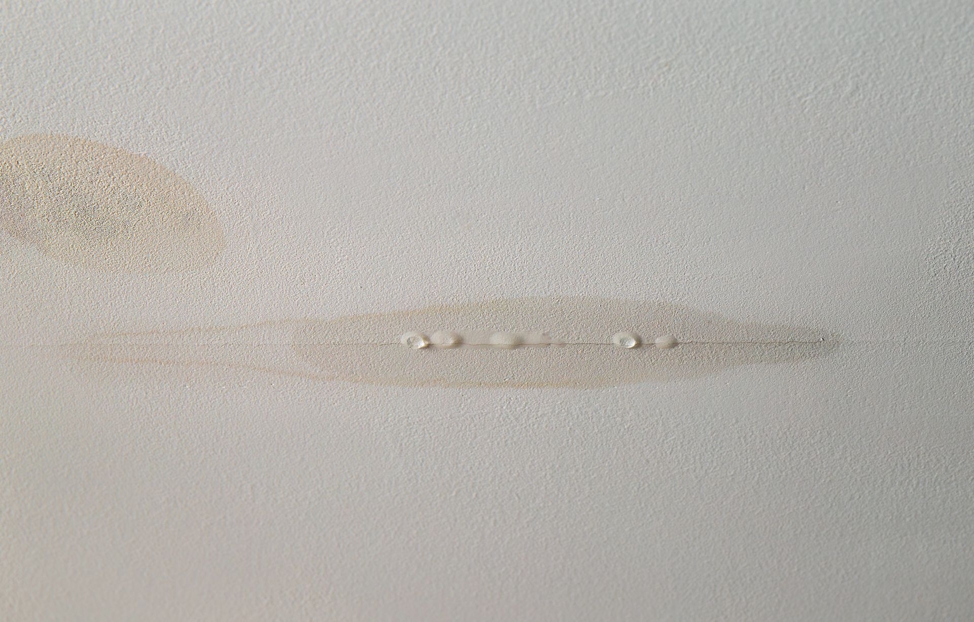 Gros plan sur un plafond blanc taché, présentant des dégâts d'eau et des zones qui s'écaillent.