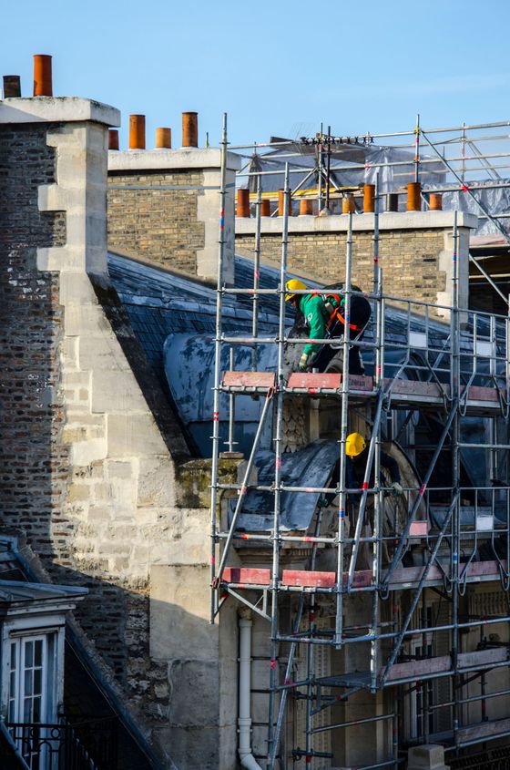 Ouvrier sur un échafaudage réparant le toit d'un bâtiment en pierre sous un ciel bleu