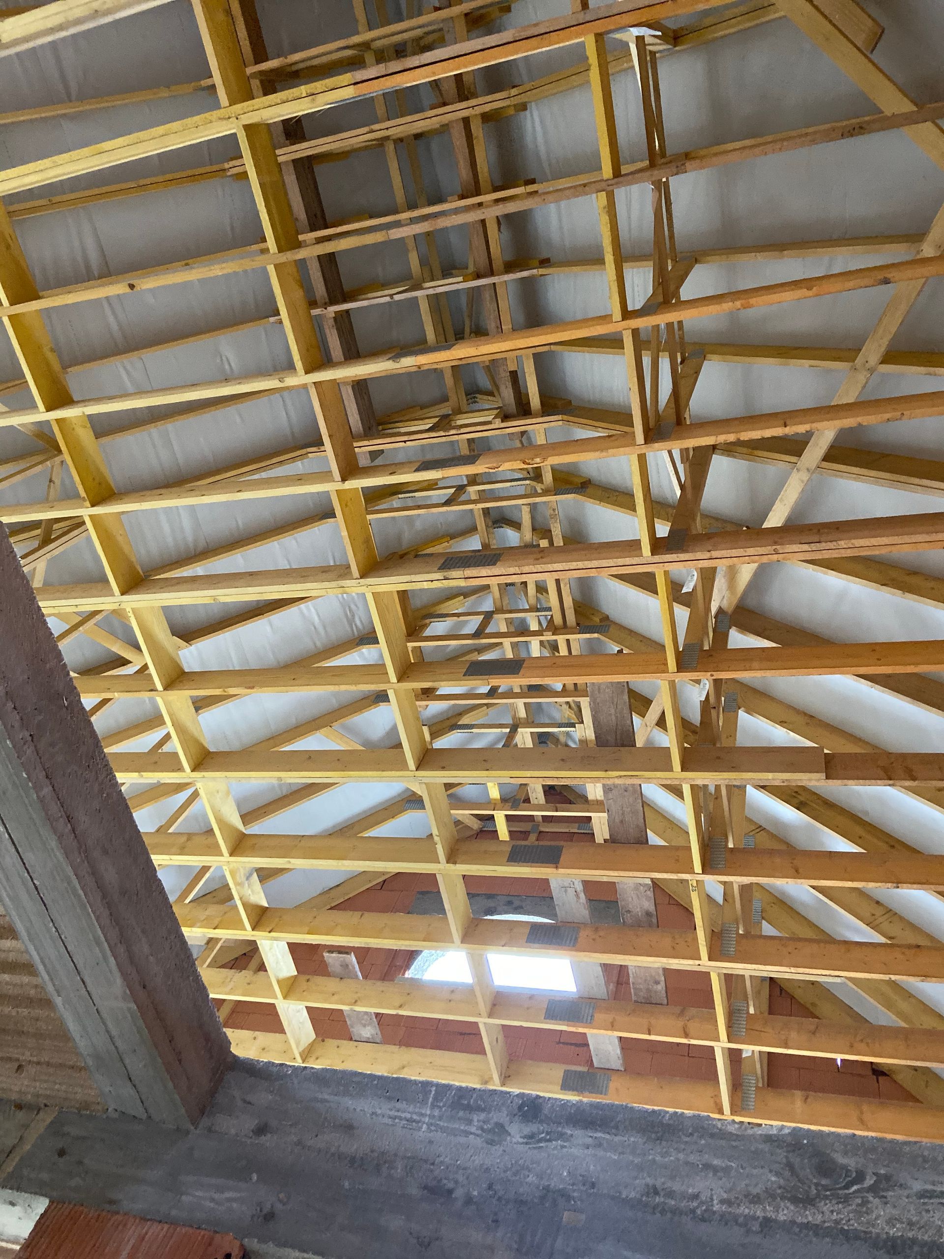 Charpente jaune à l'intérieur d'un bâtiment inachevé, avec un plafond en tôle ondulée grise et des murs en béton.