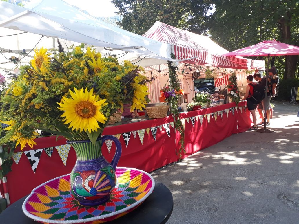 Festival Arts et Vigne - Chatillon en Diois Des barnums décorés, avec des fanions et des fleurs. 2 personnes devant le stand. Au premier plan un gros bouquet de Tournesols.