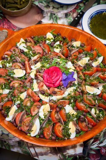 Grand saladier en bois contenant tomates, oeufs durs, haricots verts, anchois, olives noires, des fleurs au centre