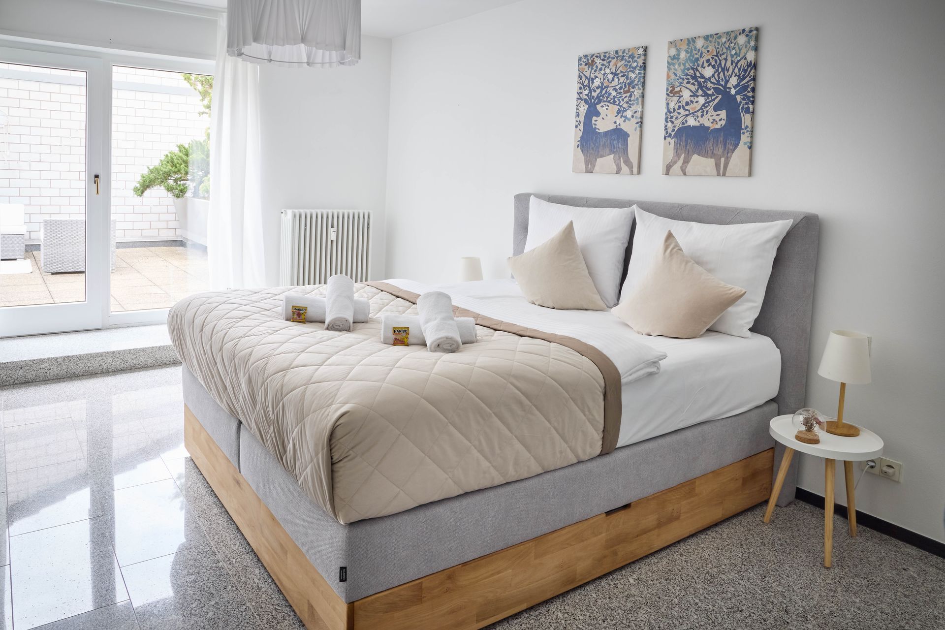Helles, modernes Schlafzimmer mit ordentlich gemachtem Bett, beigefarbener Bettwäsche und einer Sitzecke am Fenster.