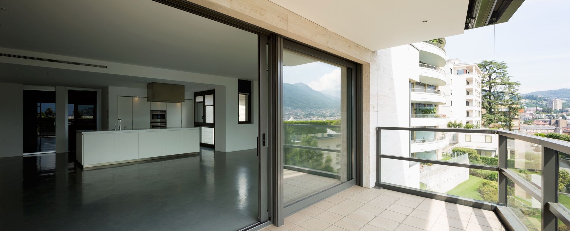Leere, moderne Wohnung mit offenem Balkon, Glasgeländer und Bergblick