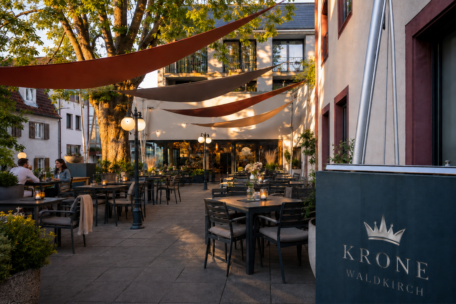 Terrasse eines Cafés im Freien mit Tischen, Stühlen und Stoffdächern neben einem Gebäude in der Abenddämmerung