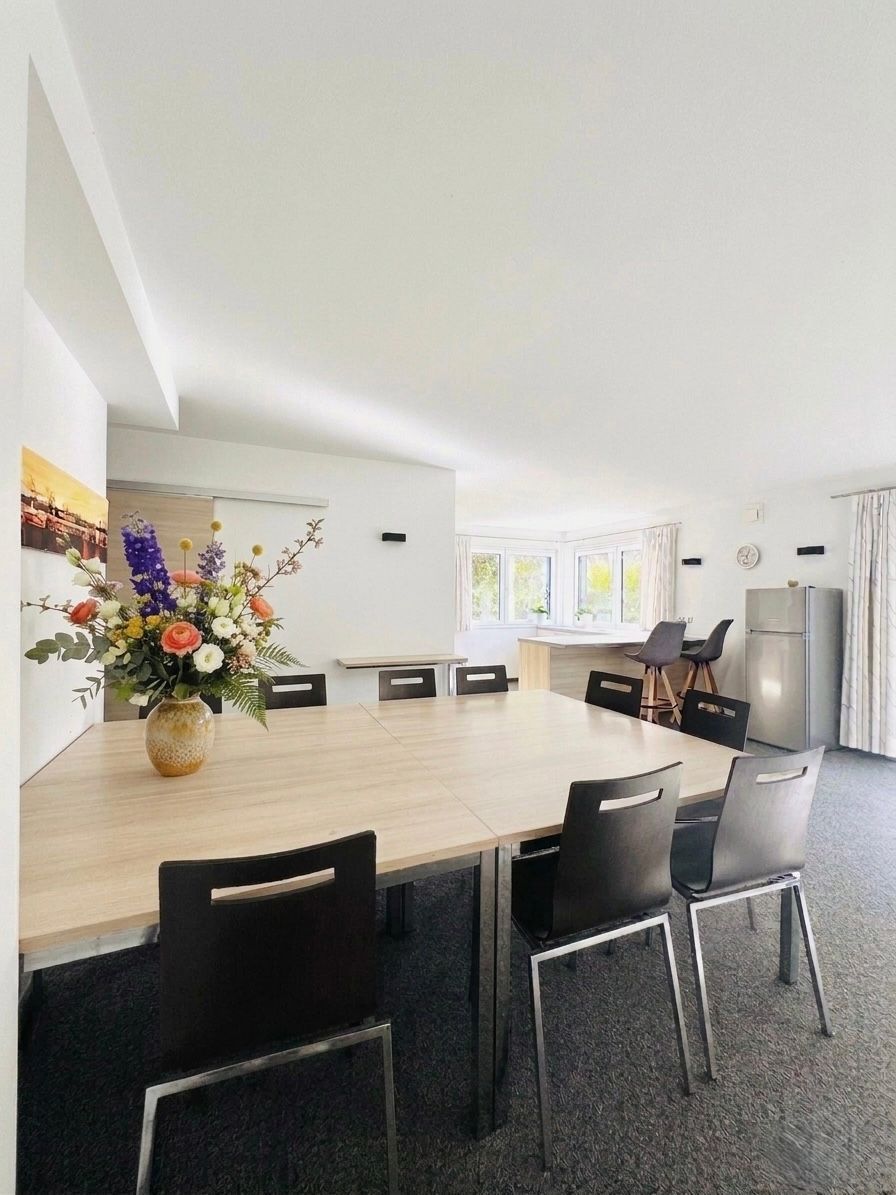 Moderne Küche mit großer Kochinsel, schwarzen Stühlen, Blumenarrangement und Edelstahlkühlschrank