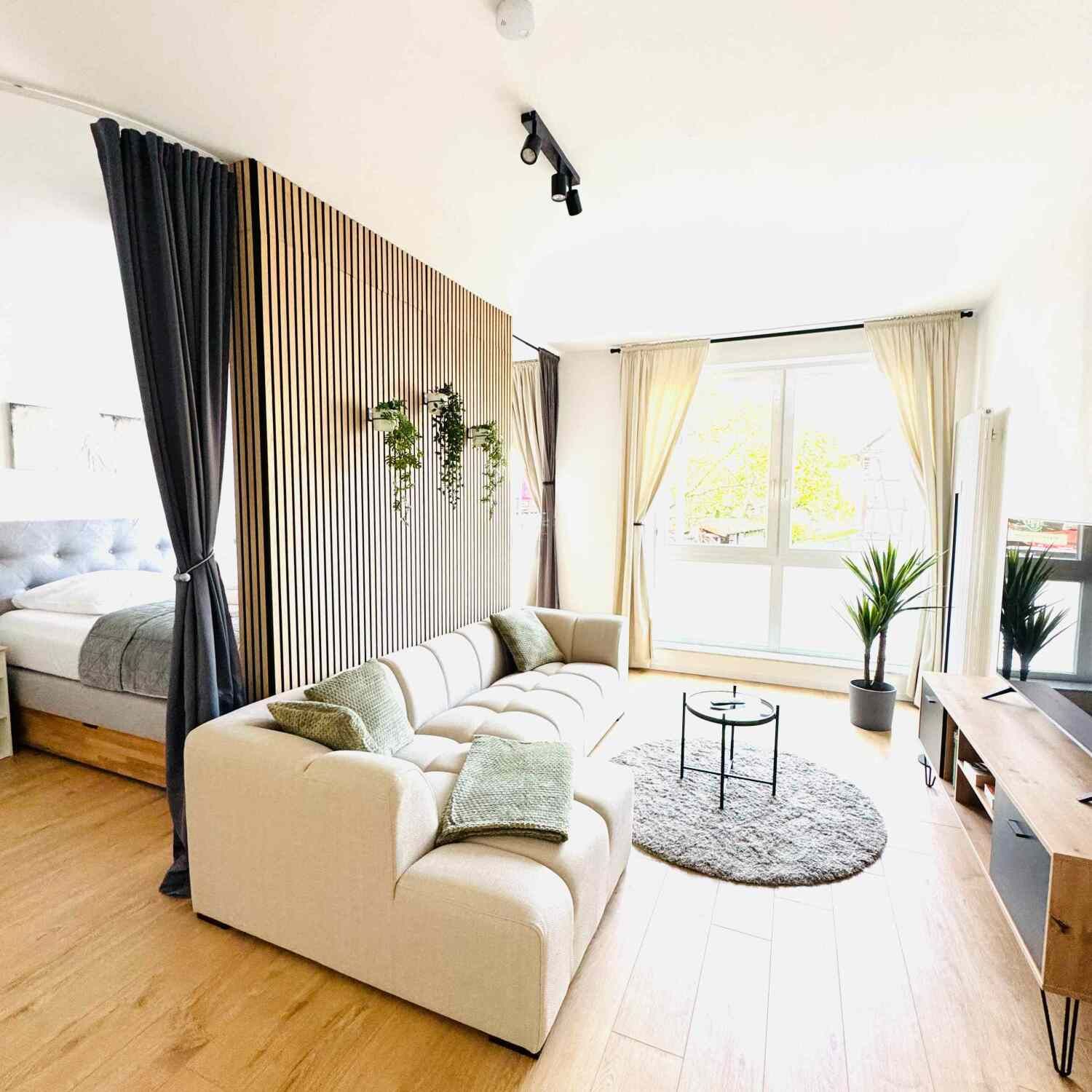 Helles, modernes Wohnzimmer mit weißem Sofa, gestreiften Vorhängen, rundem Teppich und großem Fensterlicht