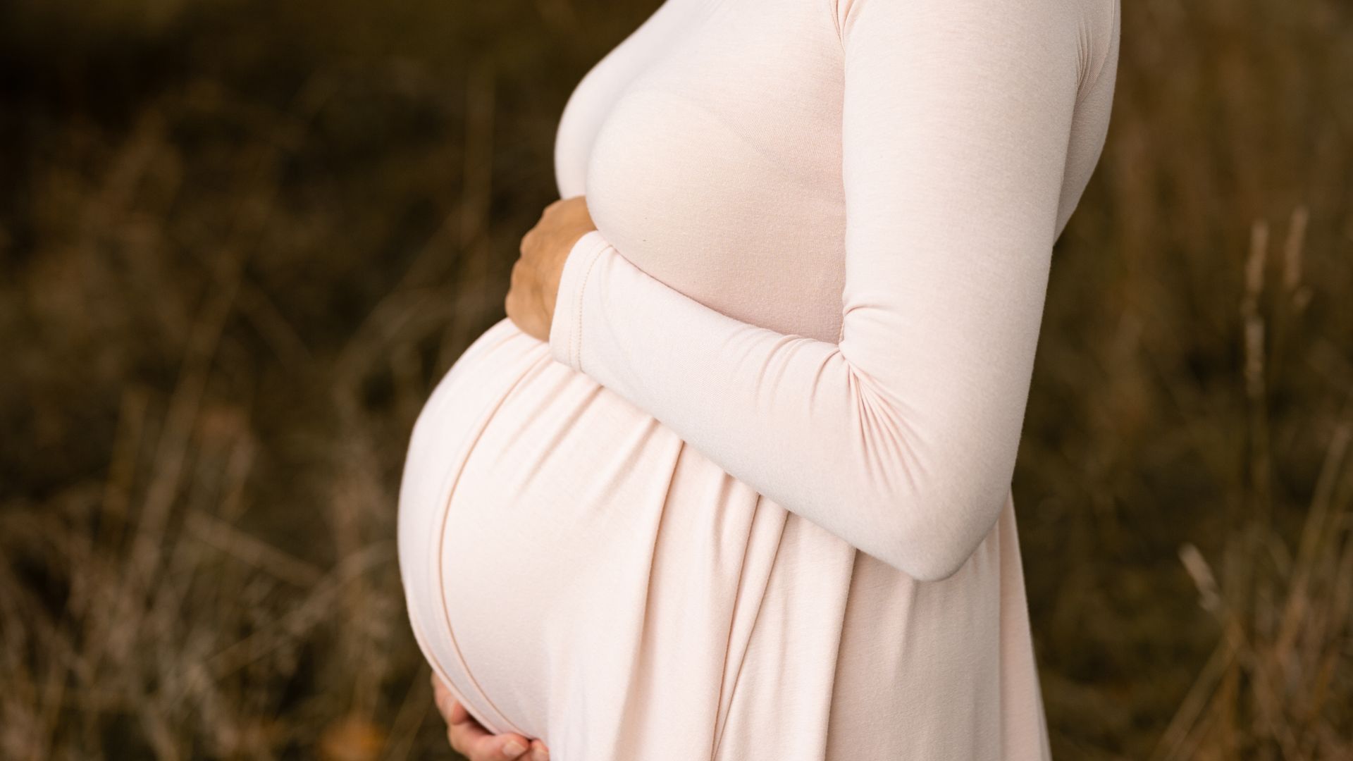 Eine schwangere Frau in einem rosa Kleid hält ihren Bauch.