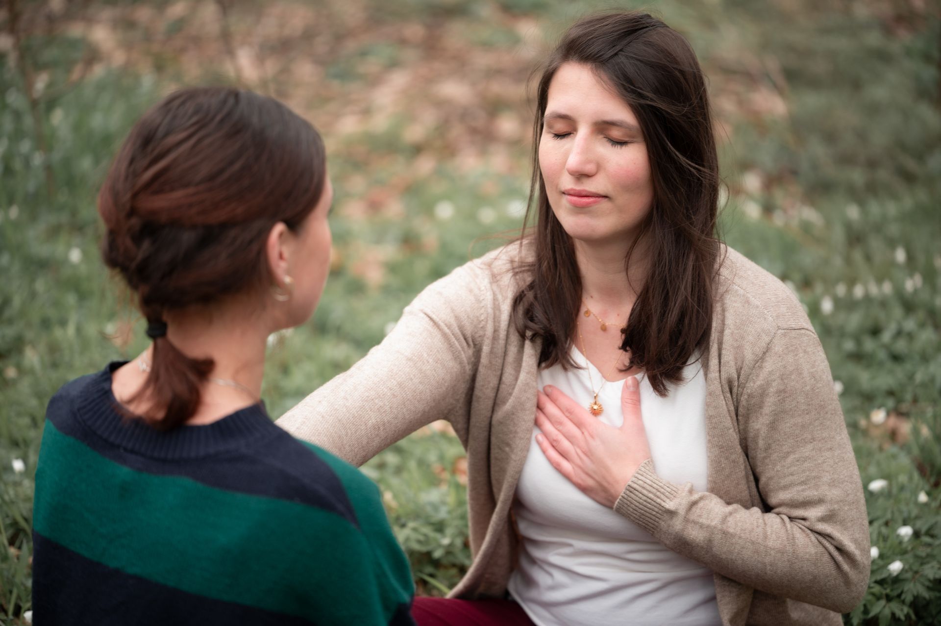 Zwei Frauen sitzen mit den Händen auf der Brust im Gras.