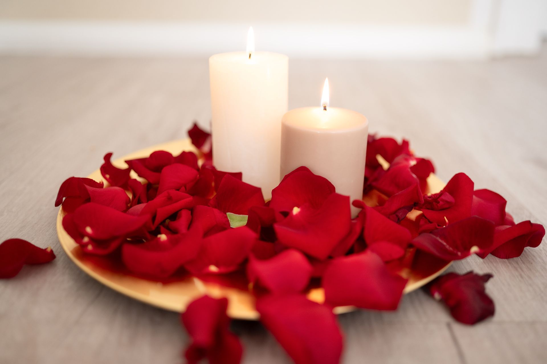 Zwei brennende Kerzen stehen auf einem Teller mit roten Rosenblättern