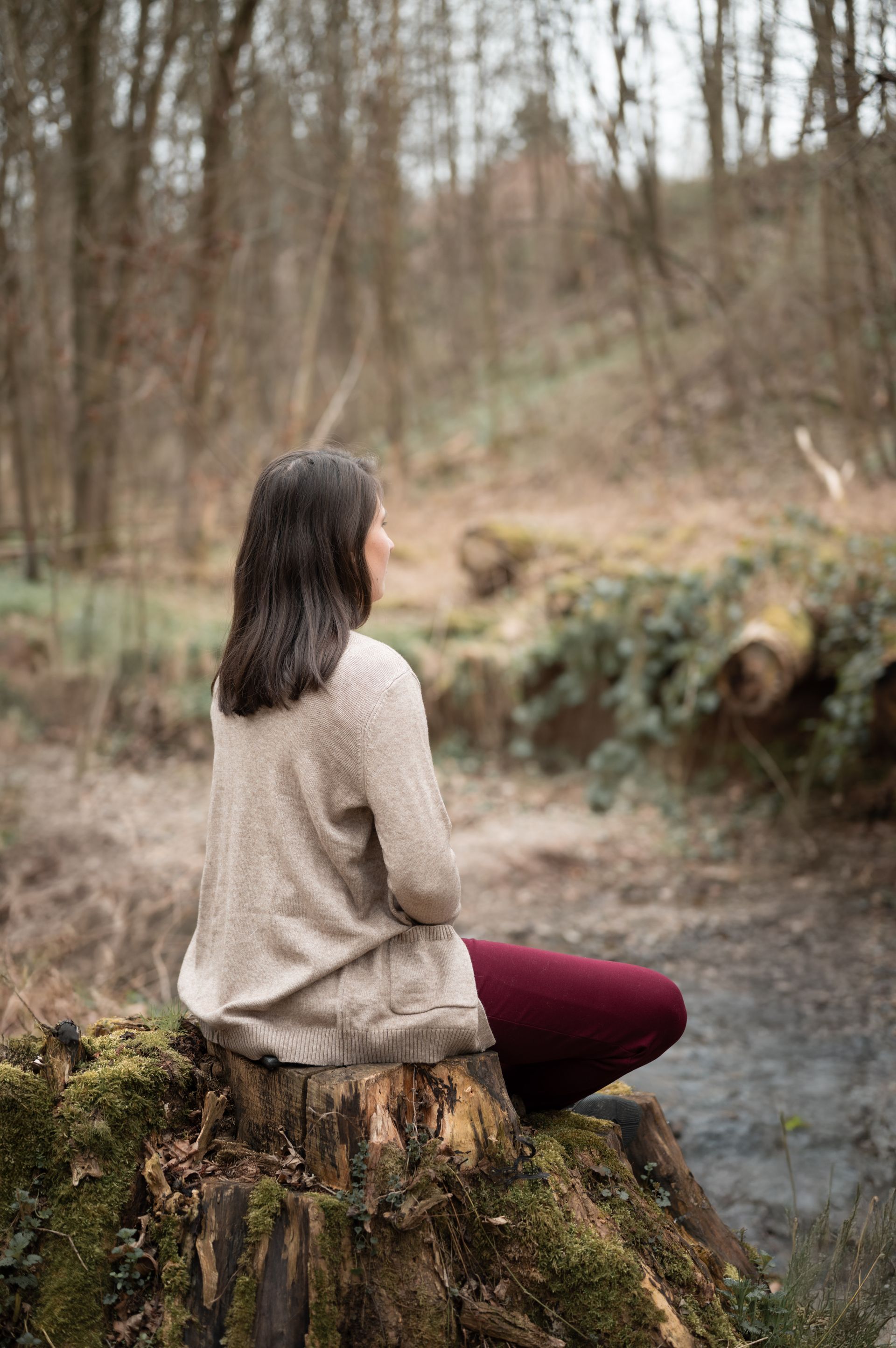 Eine Frau sitzt meditierend auf einem Baumstumpf im Wald.