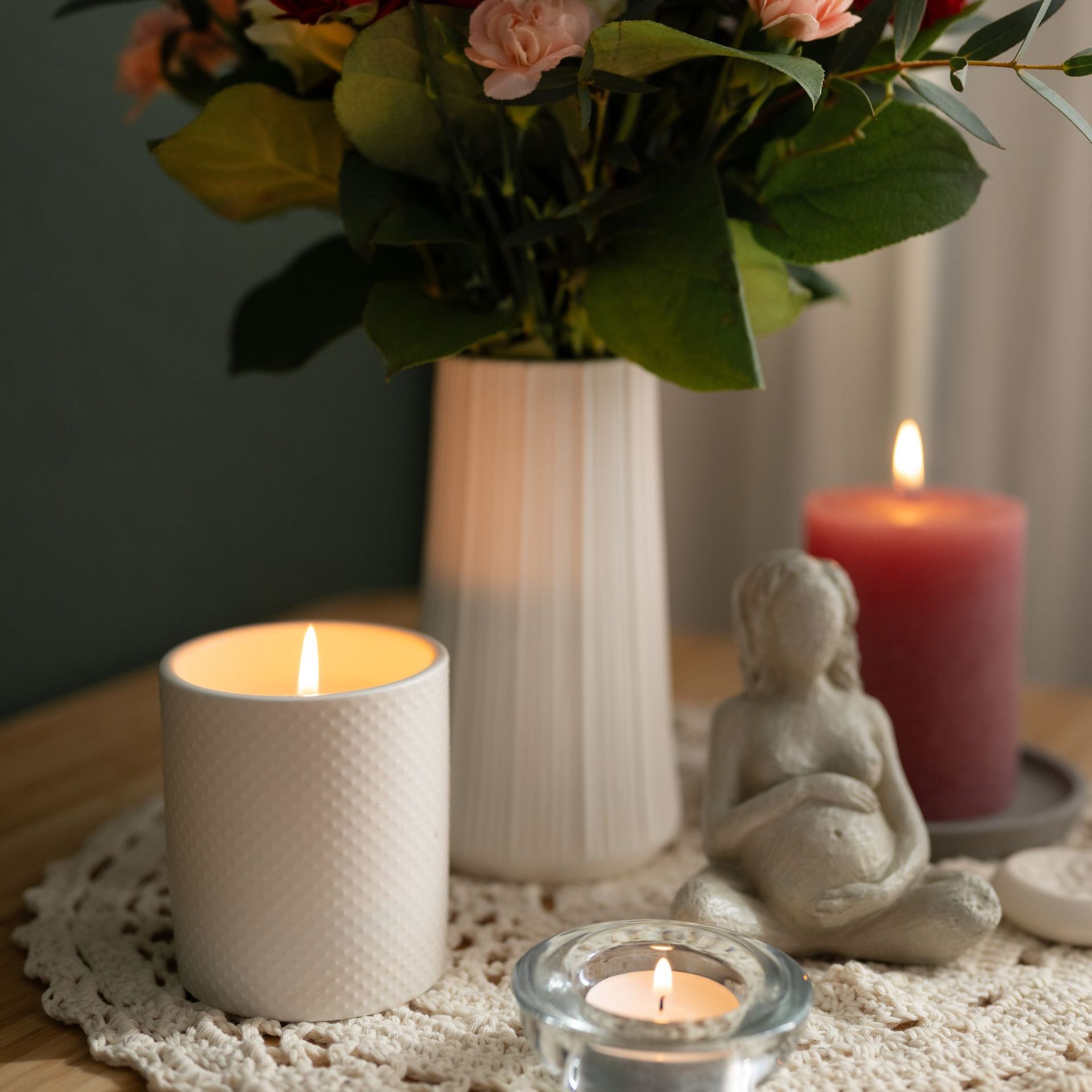 Eine Vase mit Blumen steht auf einem Tisch neben zwei brennenden Kerzen